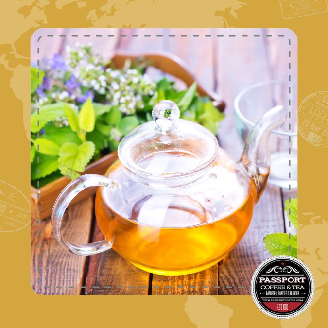 Glass teapot with Grapefruit Orange Herbal Tea on wooden table, surrounded by fresh herbs.