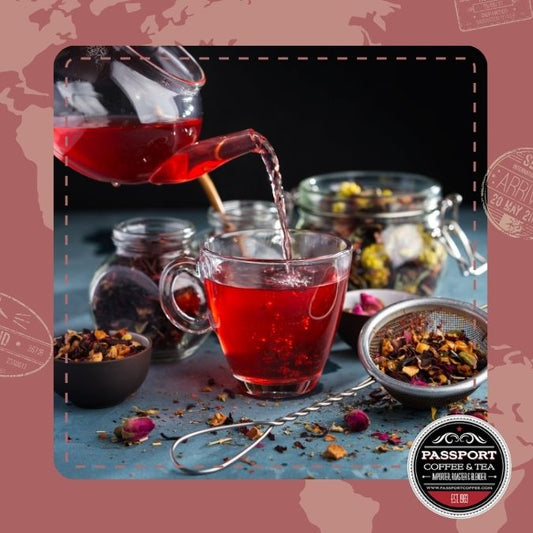 Mountain Berry Fruit Tea being poured into a glass mug with jars of dried berries and tea leaves in the background.